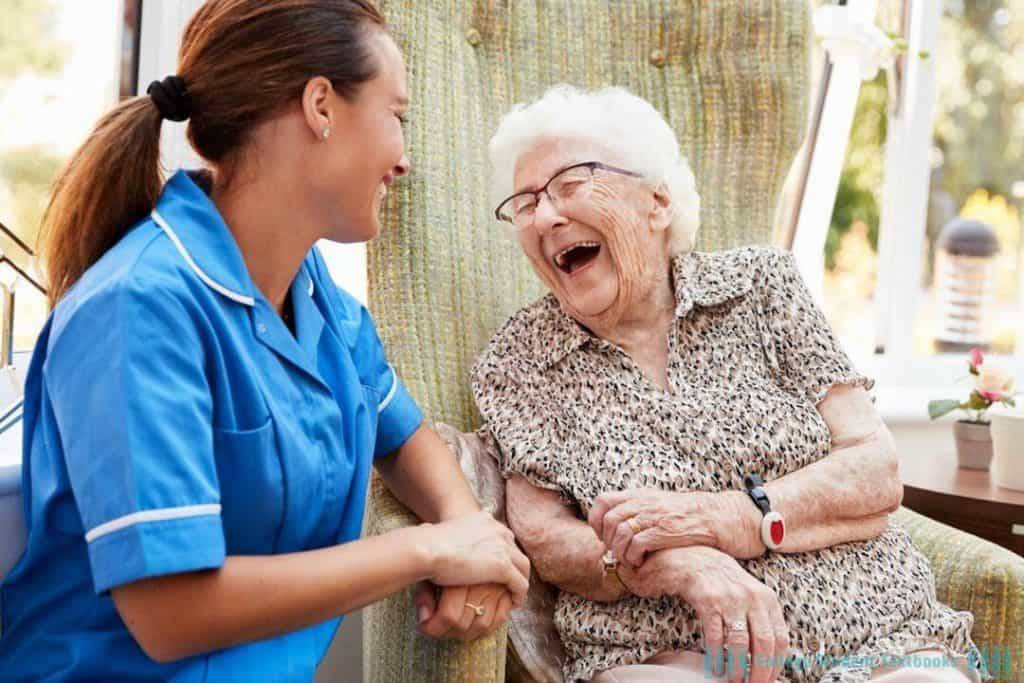 A woman caregiver smiling and talking with an elderly woman in a cozy home setting.